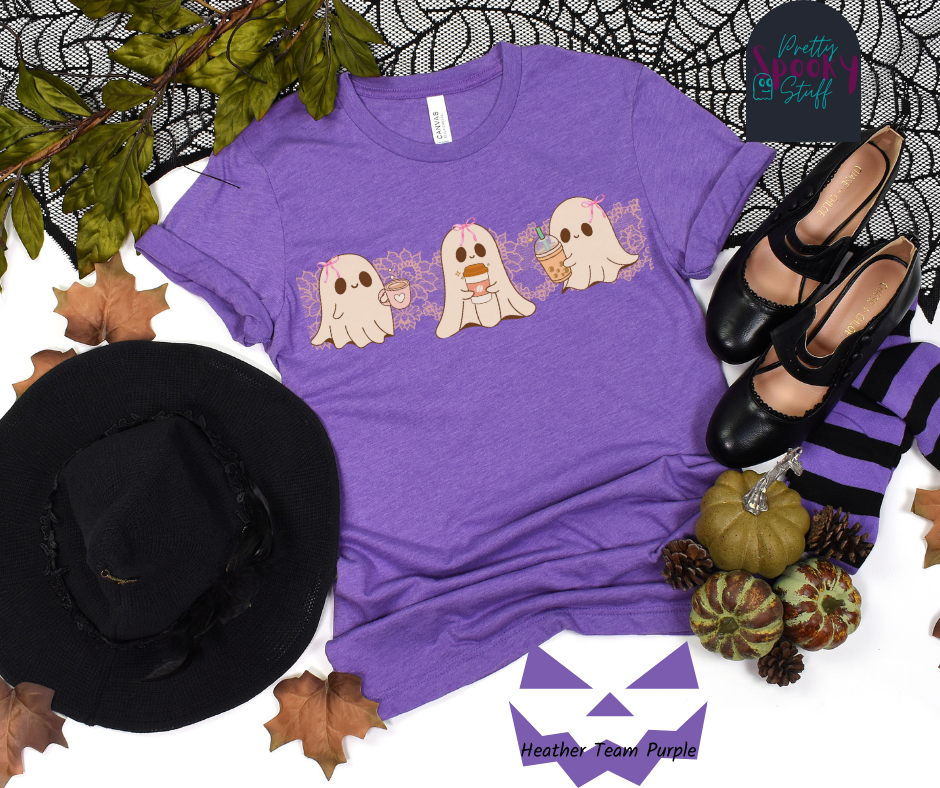 Coquette Halloween shirt with three adorable ghosts, each enjoying their own coffee beverage, adorned with a pink bow, with light pink intricate lace design behind them, in heather team purple.