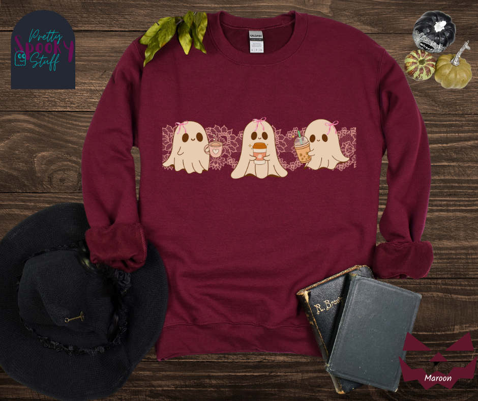 Coquette Halloween sweatshirt with three adorable ghosts, each enjoying their own coffee beverage, adorned with a pink bow, with light pink intricate lace design behind them, in maroon.