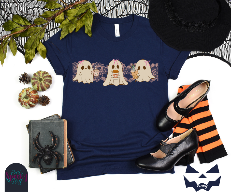 Coquette Halloween shirt with three adorable ghosts, each enjoying their own coffee beverage, adorned with a pink bow, with light pink intricate lace design behind them, in navy.