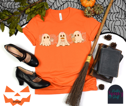 Coquette Halloween shirt with three adorable ghosts, each enjoying their own coffee beverage, adorned with a pink bow, with light pink intricate lace design behind them, in orange.