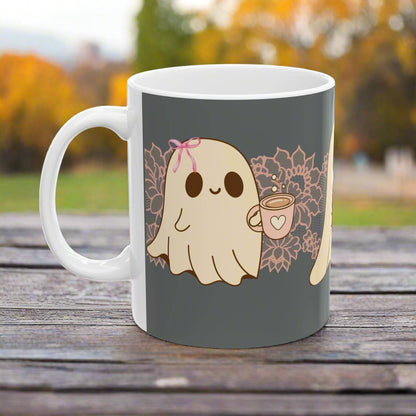 Ceramic Halloween coffee mug with three adorable ghosts, each enjoying their own coffee beverage, adorned with a pink bow, with light pink intricate lace design behind them, gray background, side view.