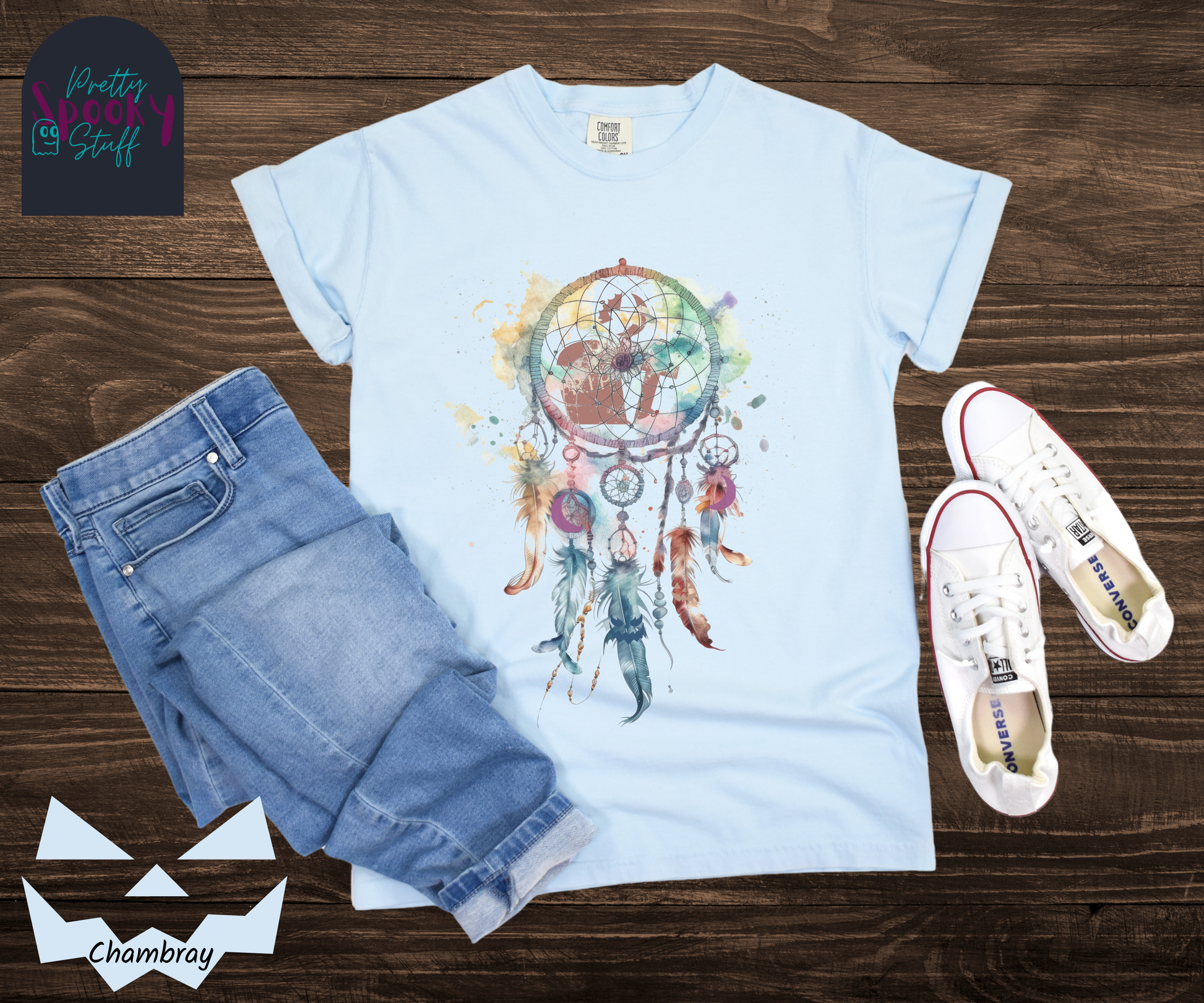Gravestone dream catcher shirt, watercolor aesthetic dream catcher with blues, pinks and purples, 5 feathers hanging blow, mauve gravestones in main circle, and crescent moons hidden in feathers, in chambray.