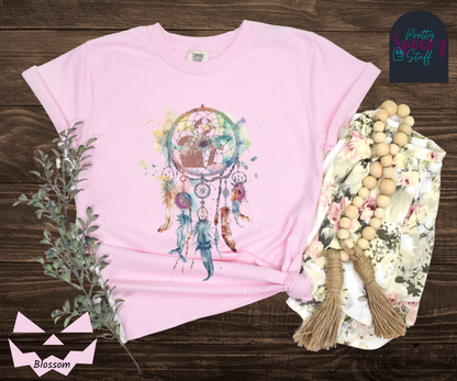 Gravestone dream catcher shirt, watercolor aesthetic dream catcher with blues, pinks and purples, 5 feathers hanging blow, mauve gravestones in main circle, and crescent moons hidden in feathers, in blossom.