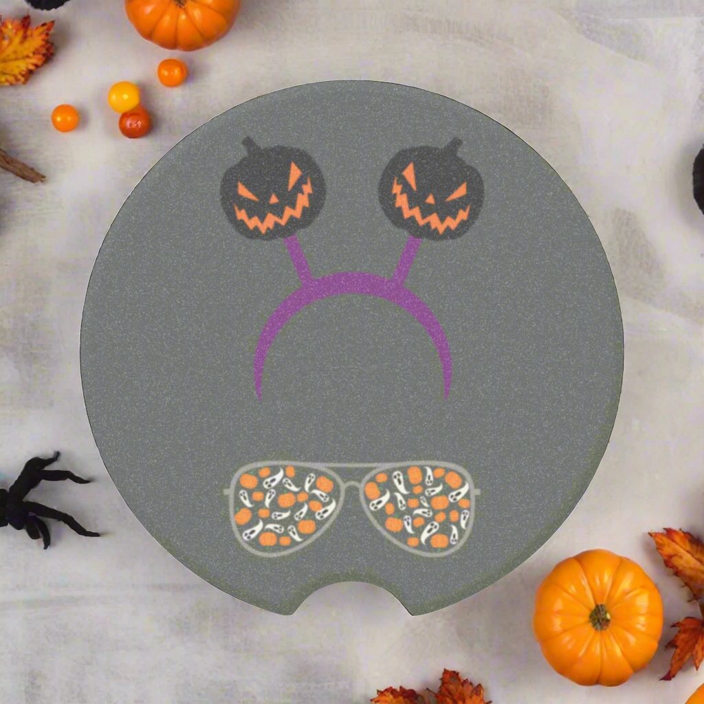 Halloween car coaster with pair of aviator glasses filled with ghosts and pumpkins in the lenses, topped with a purple headband donning dark colored jack o' lanterns, gray background.