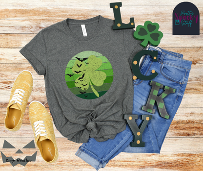 St. Patrick's Day shirt with circle green ombre lines behind light green four-leaf clover with bats flying up the left side, vintage style, in deep heather.