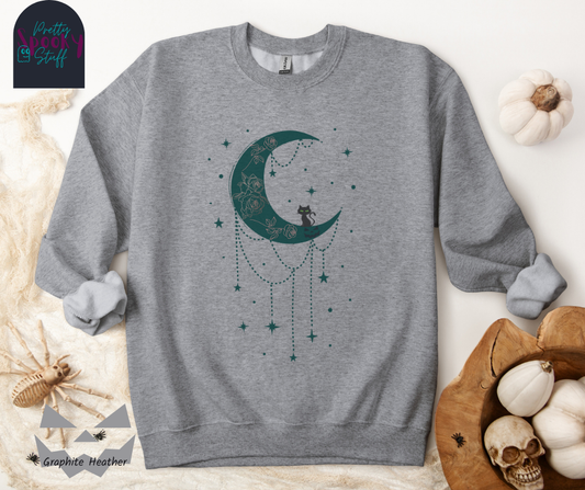 Moon and stars Halloween sweatshirt with a teal crescent moon with pink floral design inside of it, beads hanging from the bottom, a black cat perched on the bottom, and teal stars surrounding it, in graphite heather.