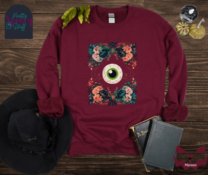Floral Halloween sweatshirt with a large eyeball in the middle, gold crescent moon and star line drawings on either side, surrounded by four bunches of flowers that make a frame, in maroon.