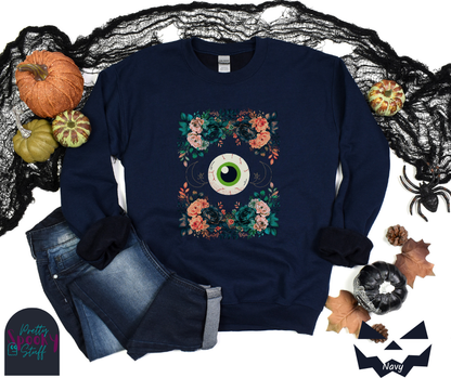 Floral Halloween sweatshirt with a large eyeball in the middle, gold crescent moon and star line drawings on either side, surrounded by four bunches of flowers that make a frame, in navy.