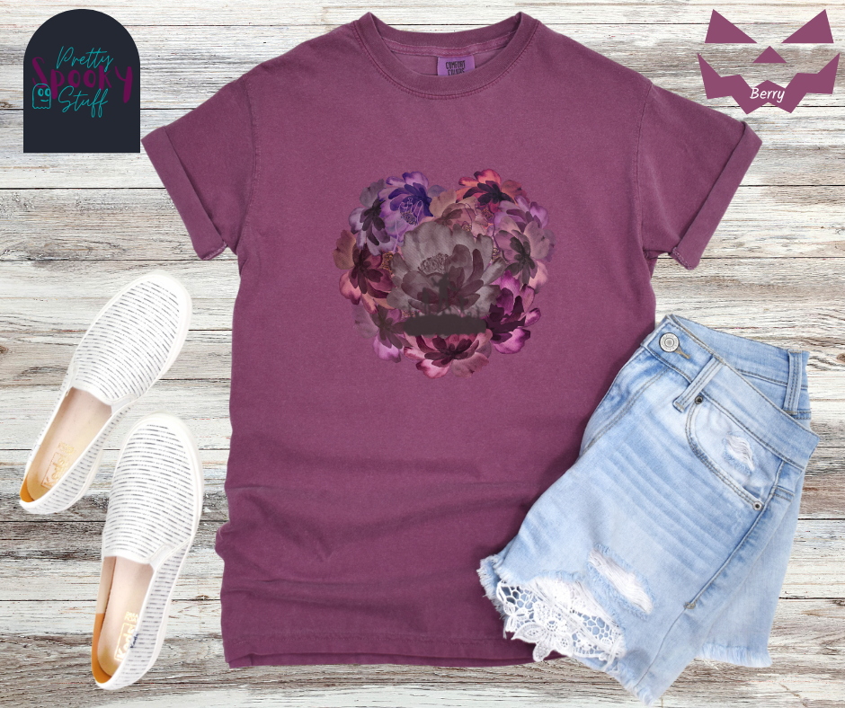 Summerween shirt with flowers of different shades of purple arranged in the shape of a heart, with shadows of running zombies and two zombie arm line drawings mixed in, in berry.