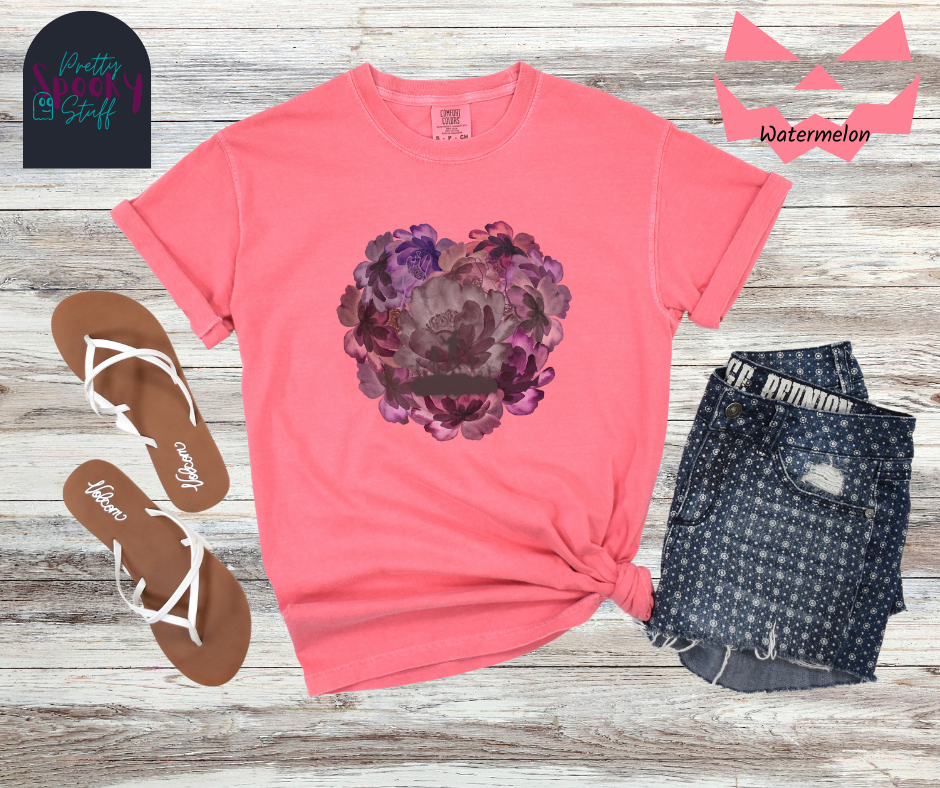 Summerween shirt with flowers of different shades of purple arranged in the shape of a heart, with shadows of running zombies and two zombie arm line drawings mixed in, in watermelon.