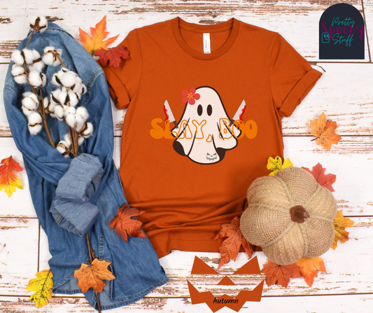 Ghost Halloween shirt with a ghost wearing pink flower, holding two bloody butcher knives and the words "slay boo" in orangle font in front of her, in autumn.
