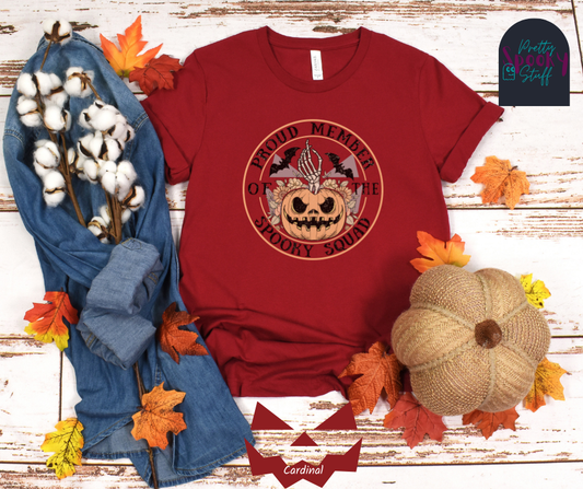 Pumpkin Halloween shirt with jack o' lantern in front of sunflowers, a skeleton hand popping out the top, two bats above, and the words "proud member of the spooky squad"  making a circle around it all, faded vintage look, in cardinal.