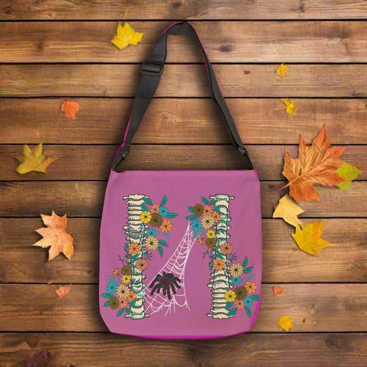 Spider Halloween tote bag with two spine bones wrapped in vintage flowers, and a tarantula spider on a web between the two, on medium purple background with black adjustable strap.