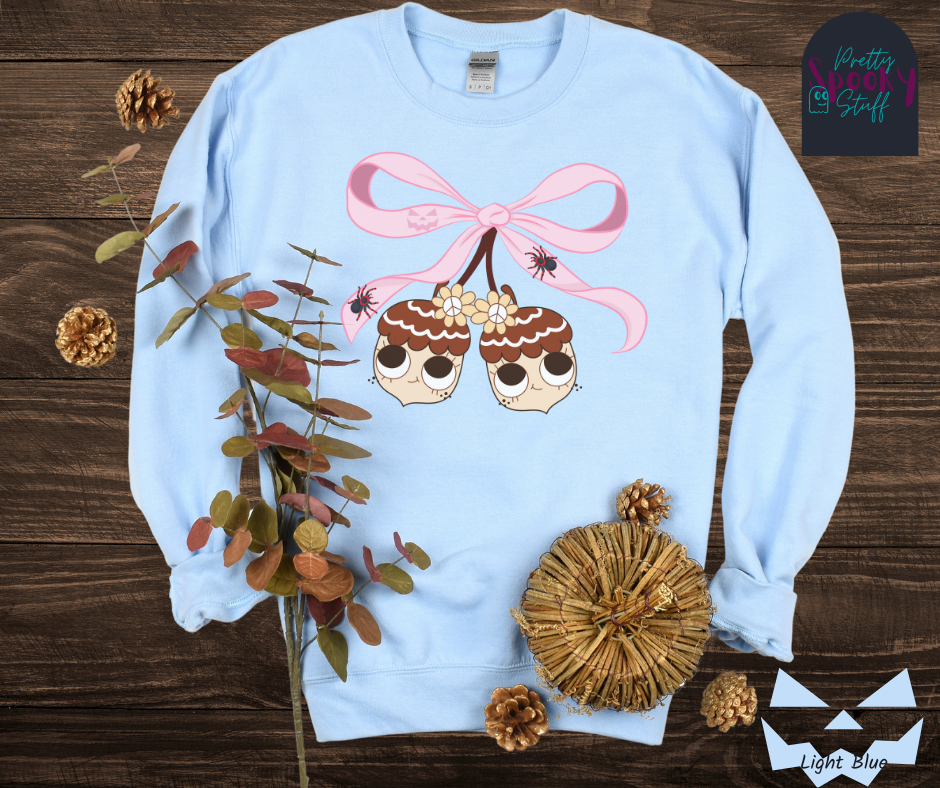 Fall coquette vintage shirt with large pink bow that ties twin acorn characters together, two spiders on the bow, acorns having cutesy faces, in light blue.