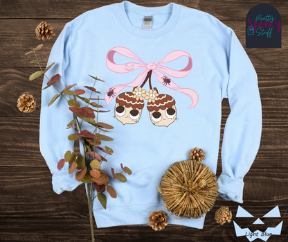 Fall coquette vintage shirt with large pink bow that ties twin acorn characters together, two spiders on the bow, acorns having cutesy faces, in light blue.