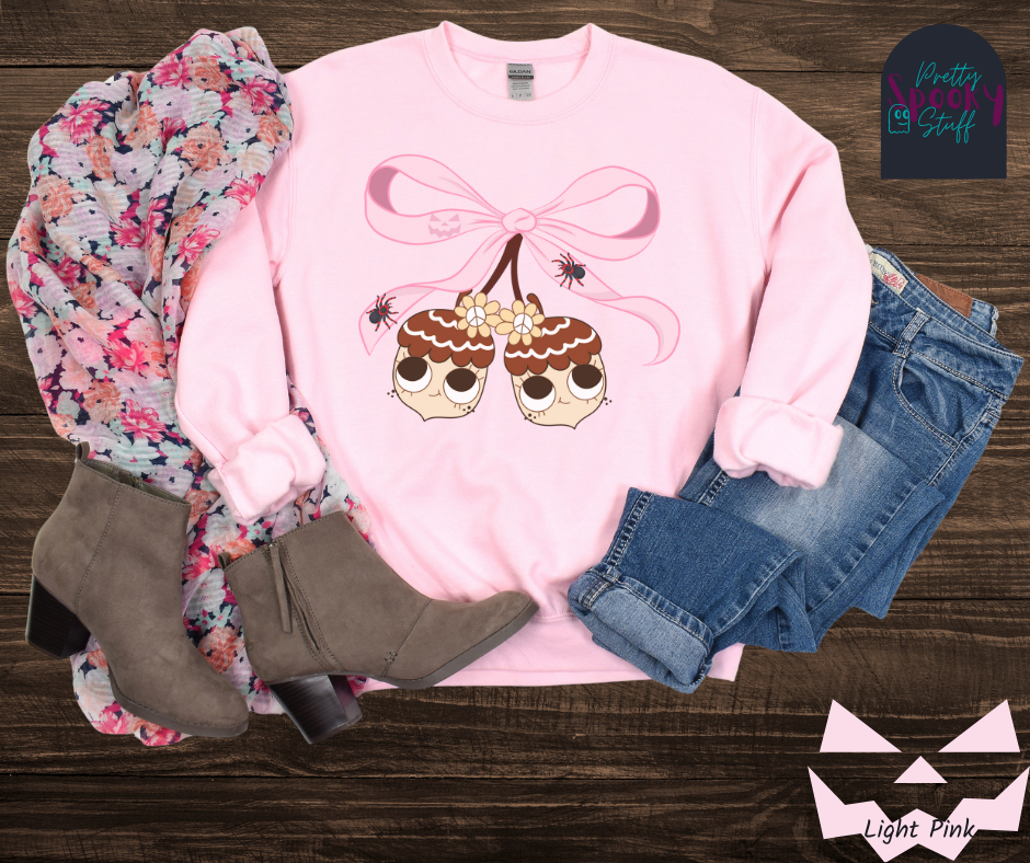 Fall coquette vintage sweatshirt with large pink bow that ties twin acorn characters together, two spiders on the bow, acorns having cutesy faces, in light pink.