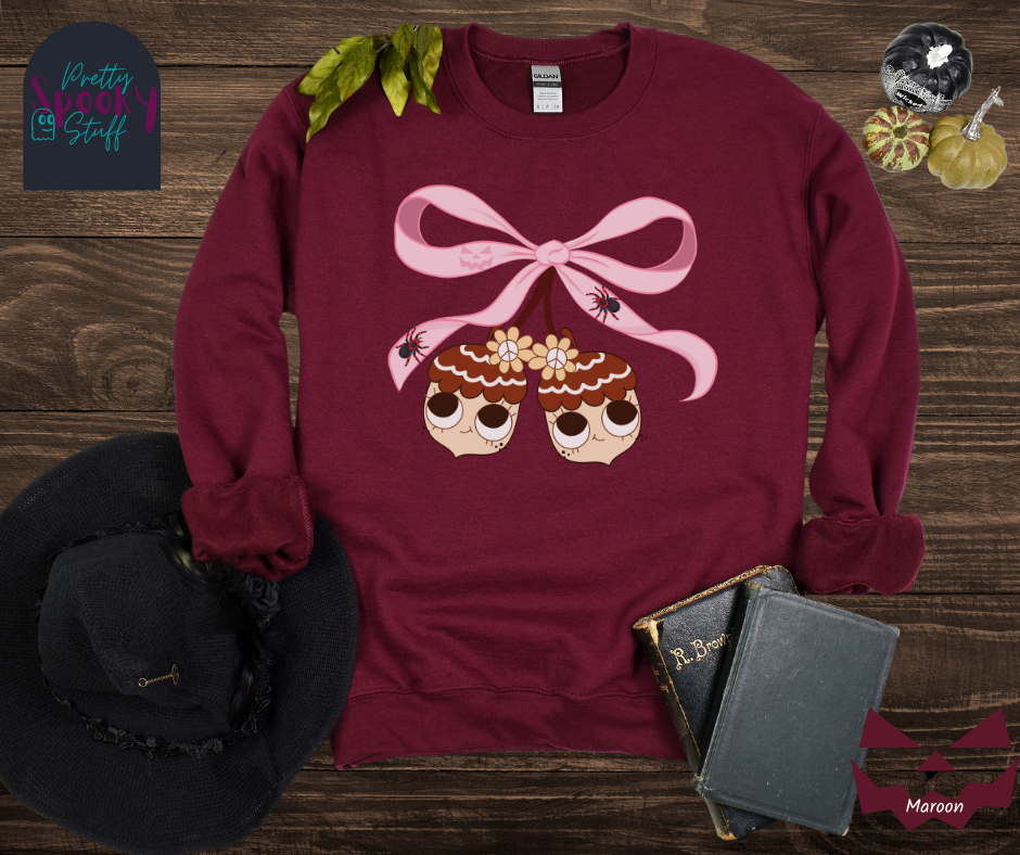 Fall coquette vintage shirt with large pink bow that ties twin acorn characters together, two spiders on the bow, acorns having cutesy faces, in maroon.