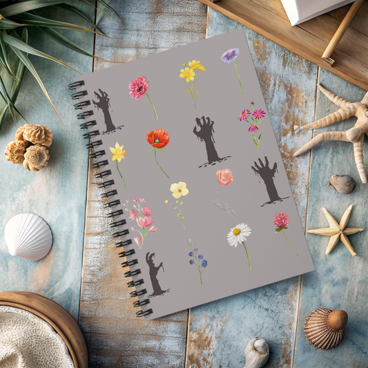 Spiral notebook with creepy zombie arms amidst different flower stems arranged in a 4 by 4 grid, on gray background, sitting on table with seashells.